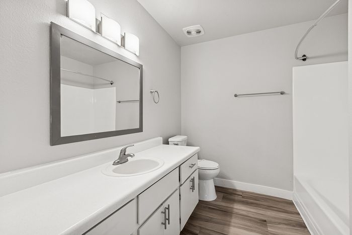 Bathroom with wood floors, shower/tub combo and white cabinets