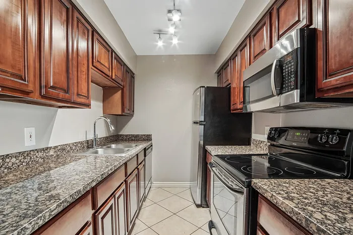 Kitchen at Solaris at The Biltmore with black/stainless appliances anf dark wood cabinets and tile flooring