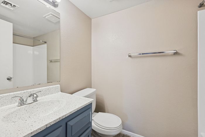Bathroom vanity with a blue cabinet, white speckled countertop, and large wall mirror.