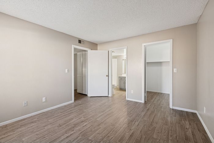 Bedroom view showing vinyl plank floors and open doors to the closet and bathroom areas.