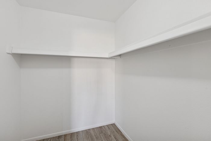 Walk-in closet with white walls and a built-in storage shelf and hanging rod.