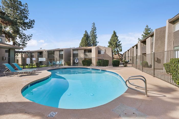 Kidney-shaped swimming pool surrounded by a fence and lounge seating.