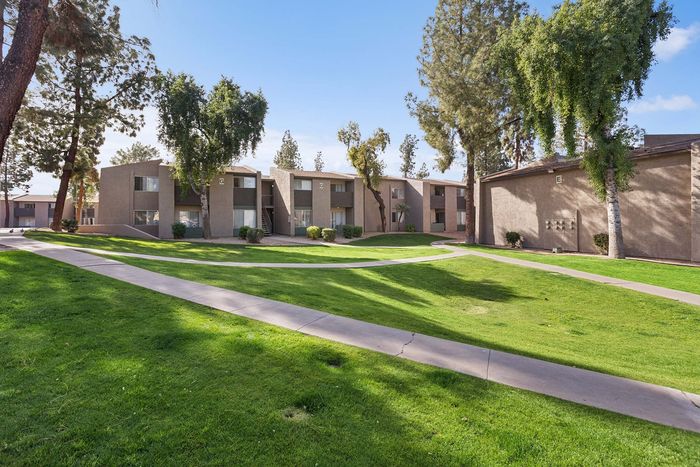 Grassy courtyard and mature trees between two-story apartment buildings at Solaris at Shadow Mountain.