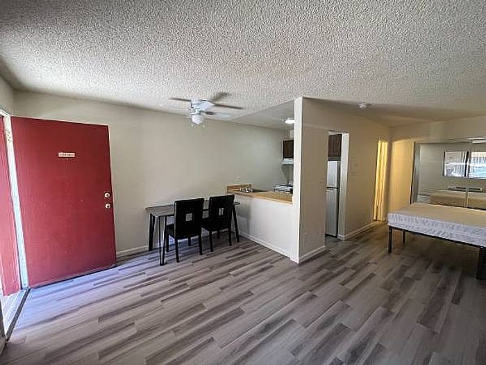 Entryway of an Ocotillo Village home showing a red door, dining set, kitchen area, and wood-style flooring.
