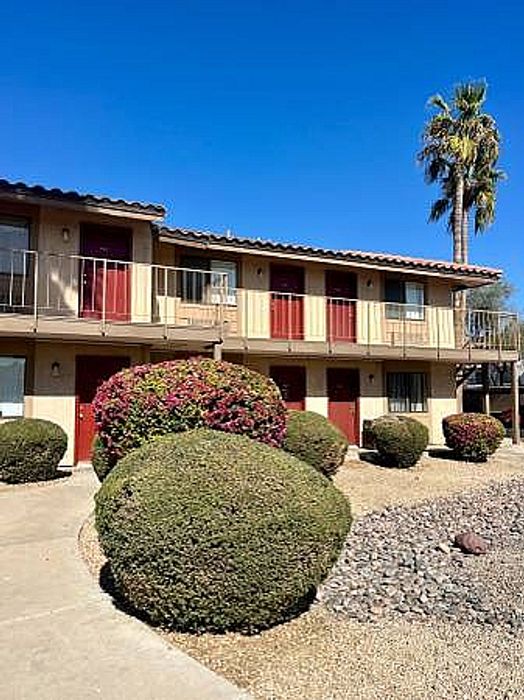 Ocotillo Village exterior featuring two-story buildings, red doors, and desert landscaping under a blue sky.