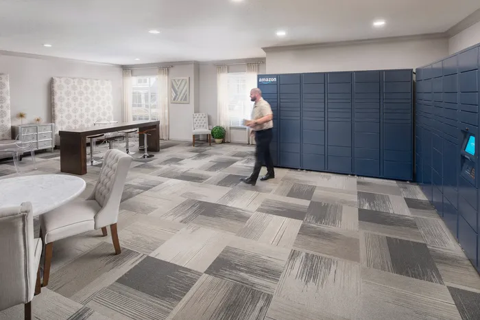 Spacious lobby with modern Amazon lockers, elegant patterned carpet, chic furniture, and natural light, perfect for a convenient and stylish living experience.