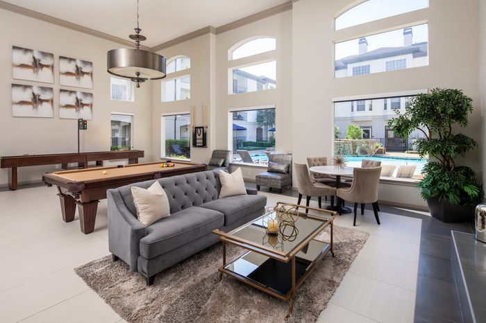Elegant apartment lounge featuring a stylish gray sofa, chic coffee table, pool table, and large windows with a view of a beautiful pool area.