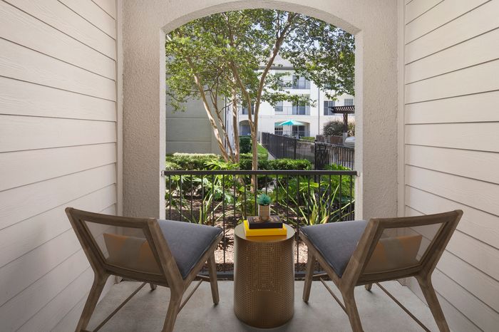 Charming apartment balcony with stylish wooden chairs, a chic table, and a lush garden view, perfect for relaxing outdoors.