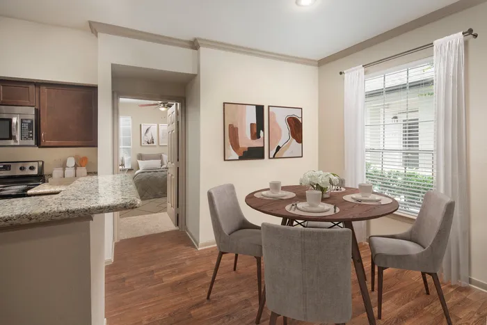 Charming dining area with a rustic wooden table, stylish gray chairs, and a cozy setting, adjacent to a modern kitchen and inviting bedroom.