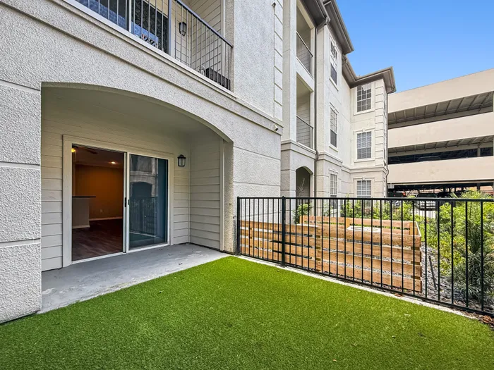 Charming apartment patio with lush green artificial turf, sliding glass door entrance, and modern architectural details.