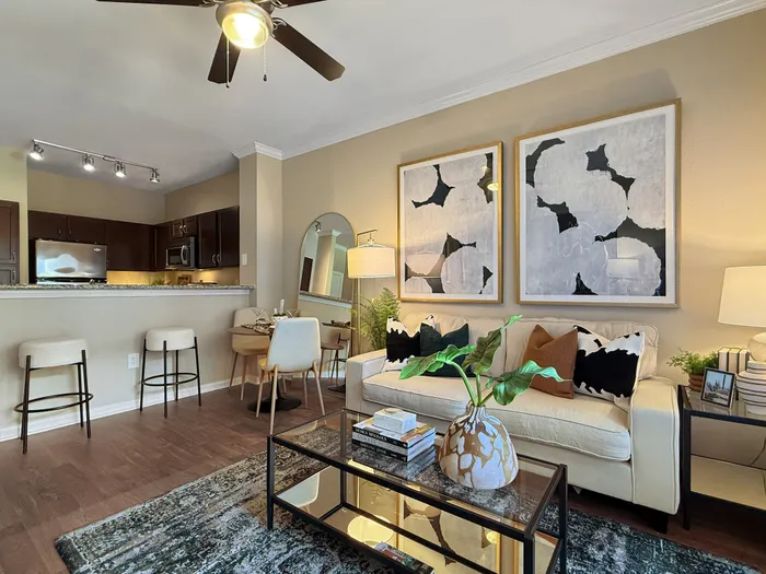 Chic living area with modern decor, a comfortable beige sofa, abstract art, and a stylish kitchen with bar seating and stainless steel appliances.