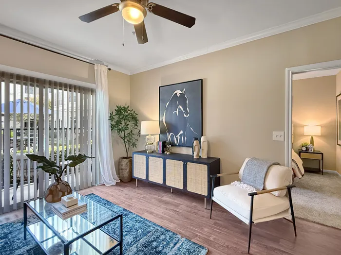 Inviting living room with elegant decor, featuring a cozy chair, vibrant area rug, and serene outdoor view through vertical blinds.