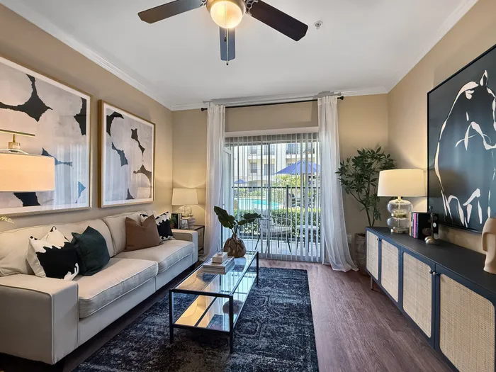 Elegant living room with modern décor, comfortable sofa, and artistic wall art, overlooking a sunlit patio with pool view.