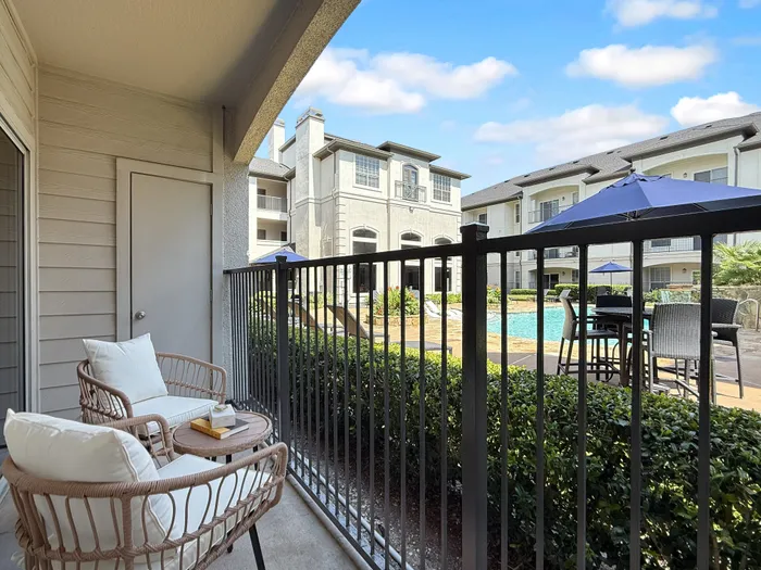 Charming apartment balcony with cozy seating overlooking a luxurious pool area and modern apartment buildings.