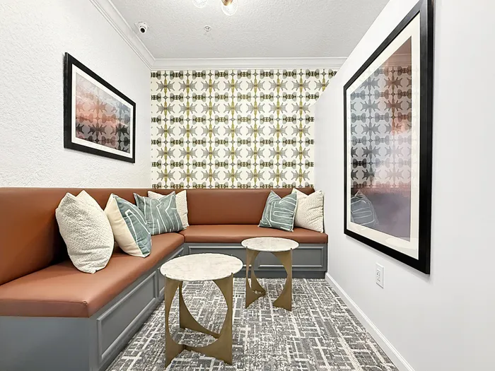 Chic apartment nook with modern orange leather seating, stylish patterned wallpaper, and elegant marble-topped tables.
