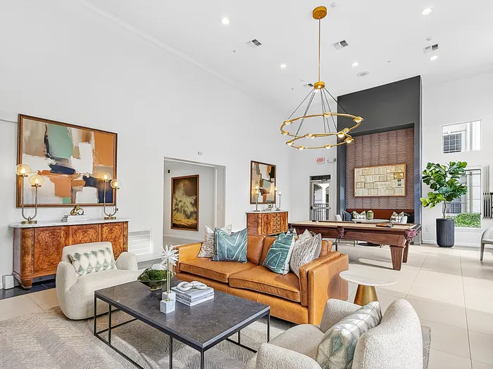 Elegant living area with modern decor featuring a plush leather sofa, chic armchairs, and a stylish pool table in a bright, open space.