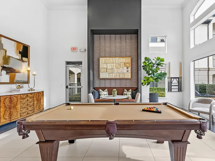 Elegant apartment lounge featuring a stylish billiard table, contemporary art, and cozy seating area with lush greenery.