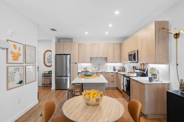 Modern kitchen with sleek wooden cabinets, stainless steel appliances, and a cozy dining area accentuated by tasteful wall art.