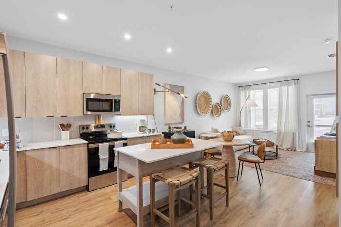 Modern open-concept kitchen and living area with sleek wooden cabinetry, stylish island seating, and abundant natural light.