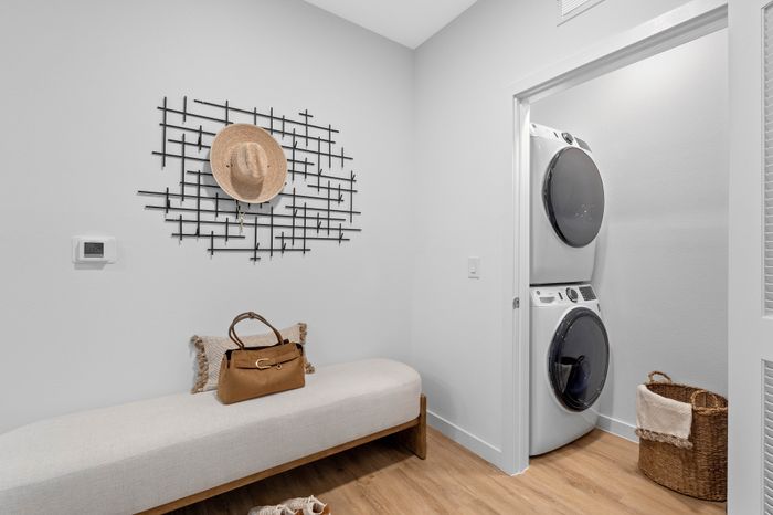 Chic laundry room with modern stacked washer and dryer, elegant wall art, and a cozy bench with stylish decor.