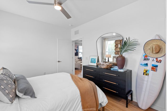 Inviting bedroom with modern ceiling fan, stylish decor, and natural light pouring in through large windows, creating a cozy and relaxing ambiance.