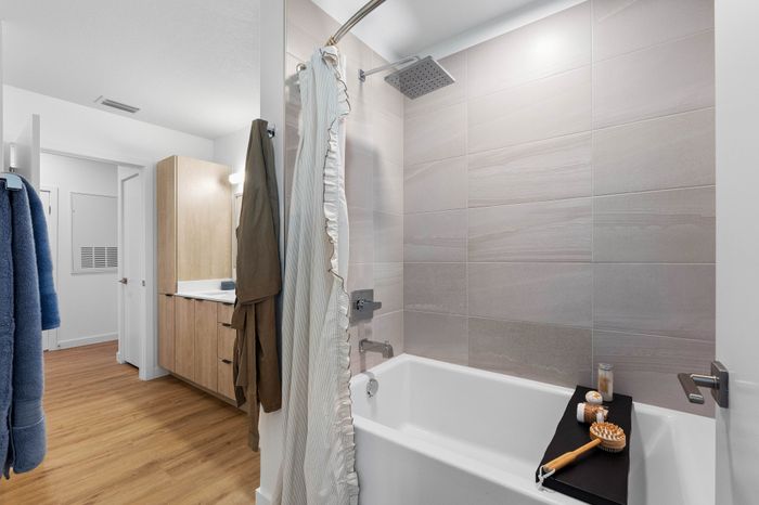 Elegant bathroom featuring a sleek shower-tub combo with luxurious rainfall showerhead, stylish wood cabinetry, and warm hardwood flooring.