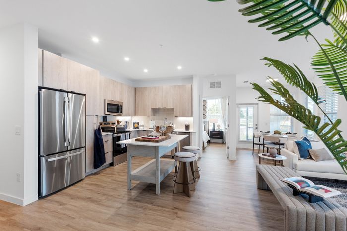 Modern open-concept kitchen and living room with sleek stainless steel appliances, stylish bar stools, and bright natural lighting.