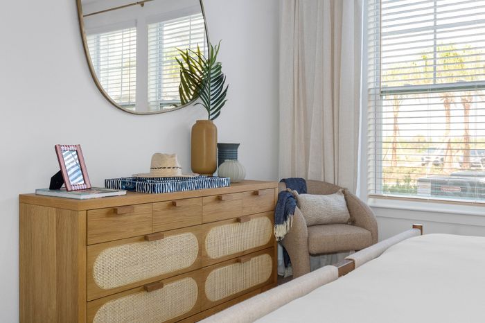 Chic bedroom corner featuring a stylish wooden dresser, cozy armchair, and large window with natural light.