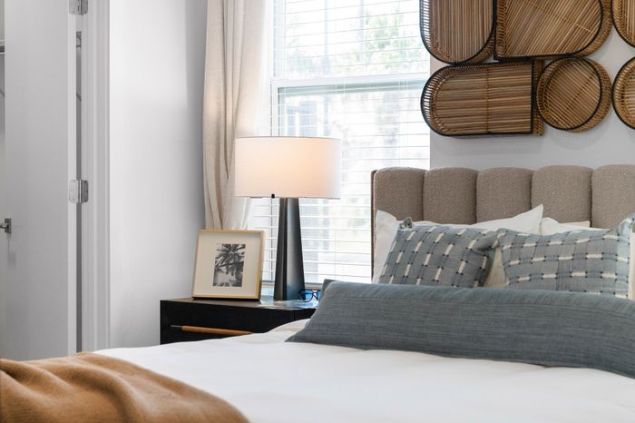 Cozy bedroom with stylish decor, featuring elegant rattan wall art, plush bedding, and a modern bedside lamp.