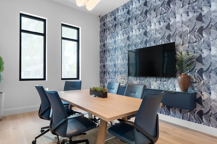 Modern conference room with stylish wallpaper, sleek wooden table, and blue ergonomic chairs, enhanced by natural light from large windows.