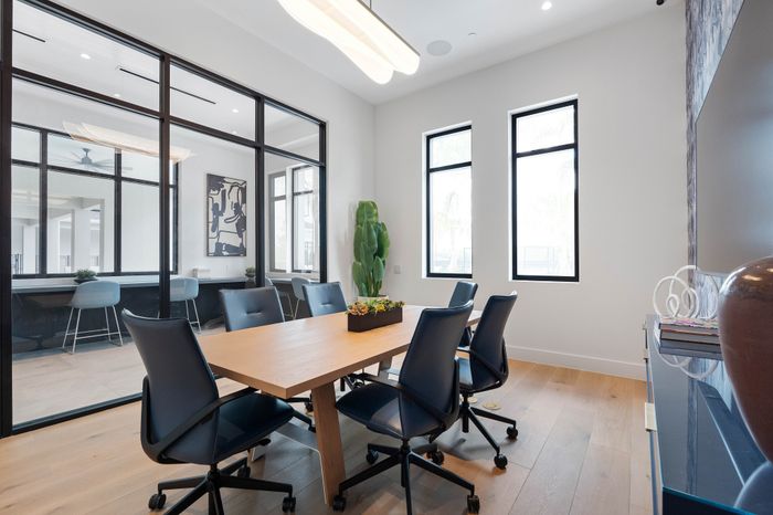 Modern conference room featuring sleek glass walls, elegant wooden table, and stylish navy chairs, bathed in natural light.