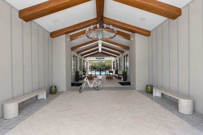 Elegant covered walkway with stylish wooden beams, decorative chandeliers, and a scenic view of a sparkling pool.