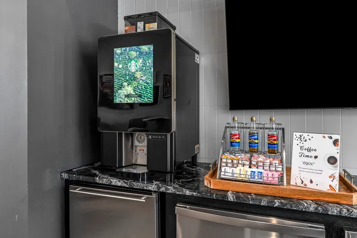 Modern coffee station featuring a sleek coffee machine and a variety of flavored syrups and creamers on a chic black marble countertop.