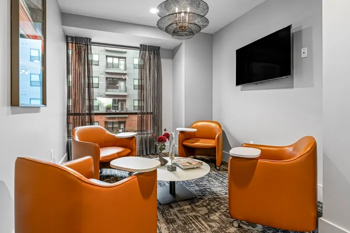 Chic seating area with bright orange chairs, modern decor, and a large window offering city views.