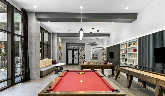Luxurious apartment recreation room with red pool table, modern lighting, cozy seating area, and stylish bookshelves, ideal for entertainment and relaxation.