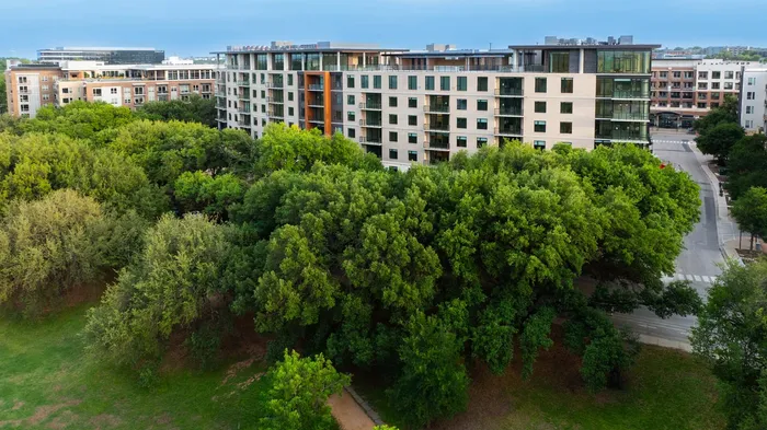 Modern apartment complex with a sleek exterior set amidst lush greenery and urban surroundings.
