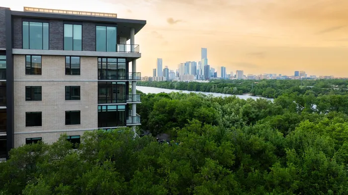 Modern apartment building with expansive windows overlooking lush greenery and a vibrant cityscape under a golden sky.