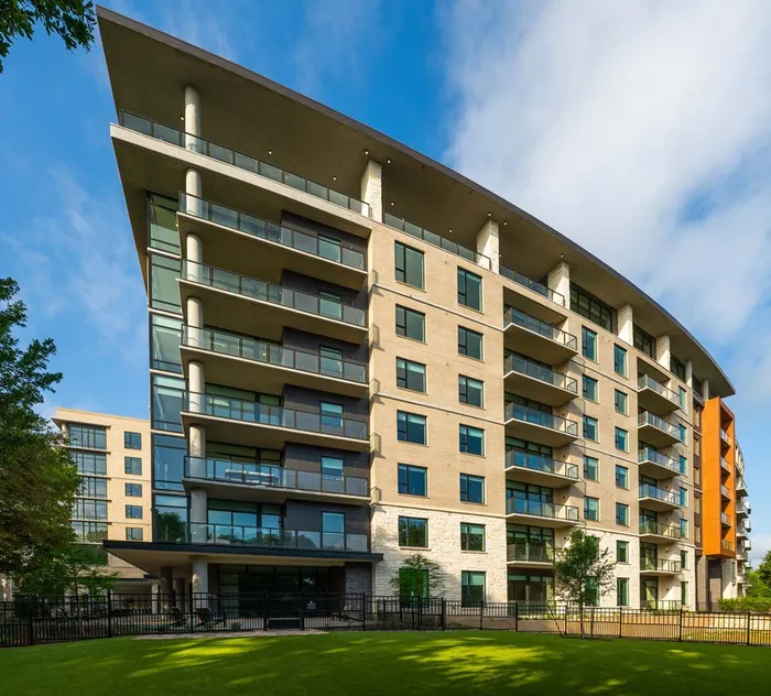 Contemporary apartment building with spacious balconies, floor-to-ceiling windows, and a sleek modern design against a clear blue sky.