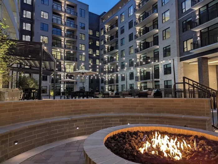 Elegant apartment courtyard illuminated by string lights, with cozy fire pit and modern patio seating.