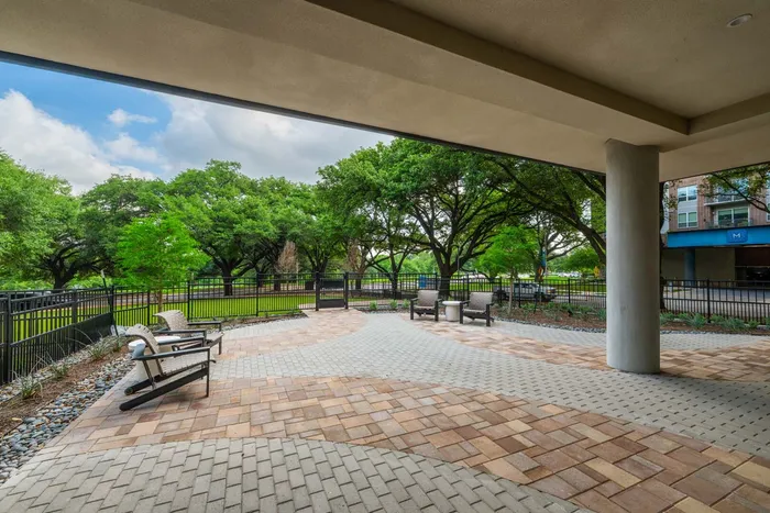 Inviting apartment patio with stylish paving, comfortable seating, and lush greenery under a bright blue sky.