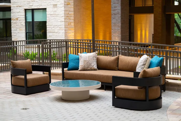 Modern outdoor seating area with a stylish brown couch, elegant black frame chairs, and a round glass-top table on a chic patio.