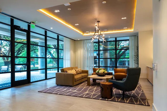 Modern apartment lobby with floor-to-ceiling windows, cozy seating, and contemporary lighting, creating an inviting atmosphere.