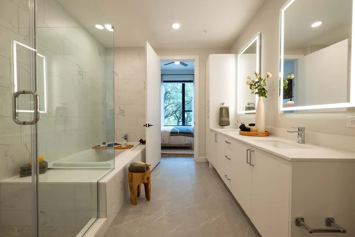 Modern bathroom with elegant marble tiles, dual vanity with mirrors, and a glass-enclosed shower, exuding luxury and comfort.