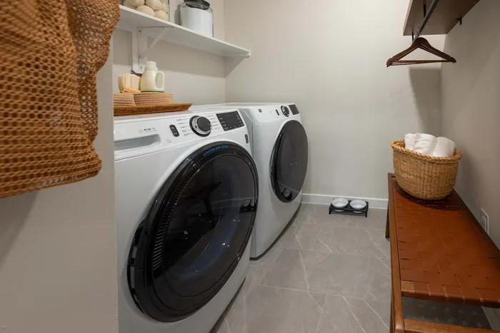 Chic laundry room featuring modern washer and dryer, stylish shelving, and cozy woven accents.
