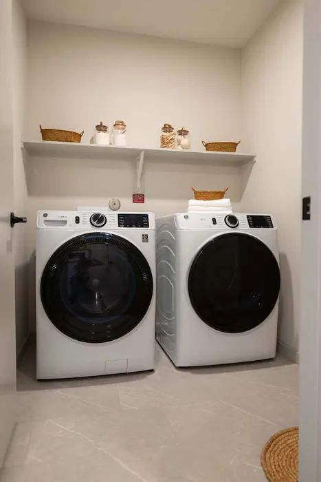 Modern laundry room featuring sleek front-load washer and dryer with stylish shelving and decorative baskets.