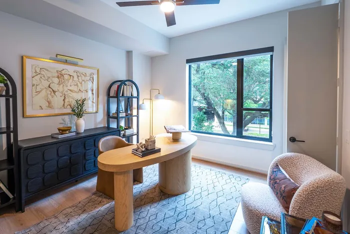 Elegant home office with a sleek wooden desk, cozy armchair, and large window offering a serene view of greenery.