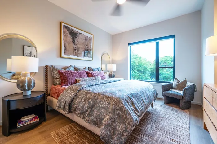 Chic bedroom adorned with elegant decor, featuring a luxurious bed, modern artwork, and abundant natural light from a large window.