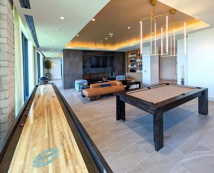 Luxurious game room featuring a sleek pool table and shuffleboard, elegant lighting, modern seating, and entertainment options.