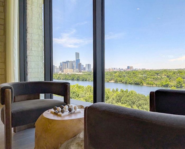 Luxurious apartment view showcasing a stunning city skyline and tranquil river, framed by modern, elegant furnishings.