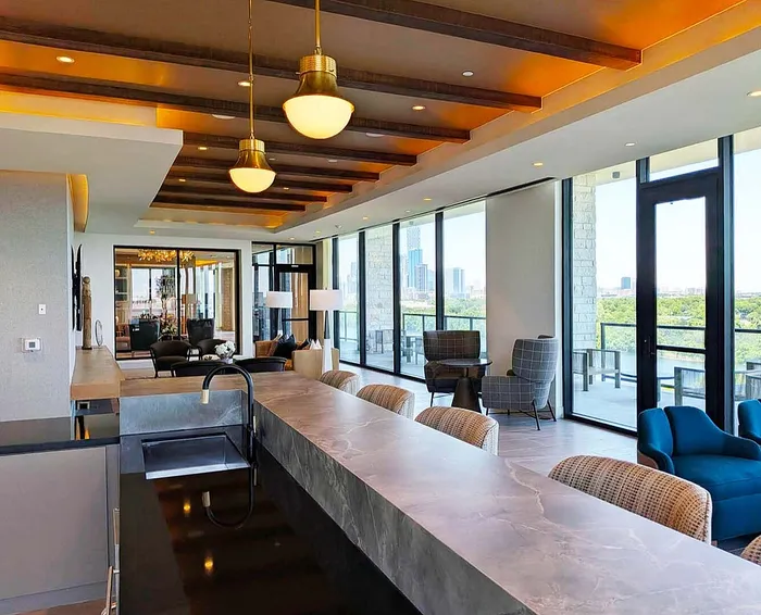 Luxurious apartment interior with an open-concept layout, featuring a sleek kitchen island, stylish lighting, and expansive floor-to-ceiling windows offering a stunning city view.